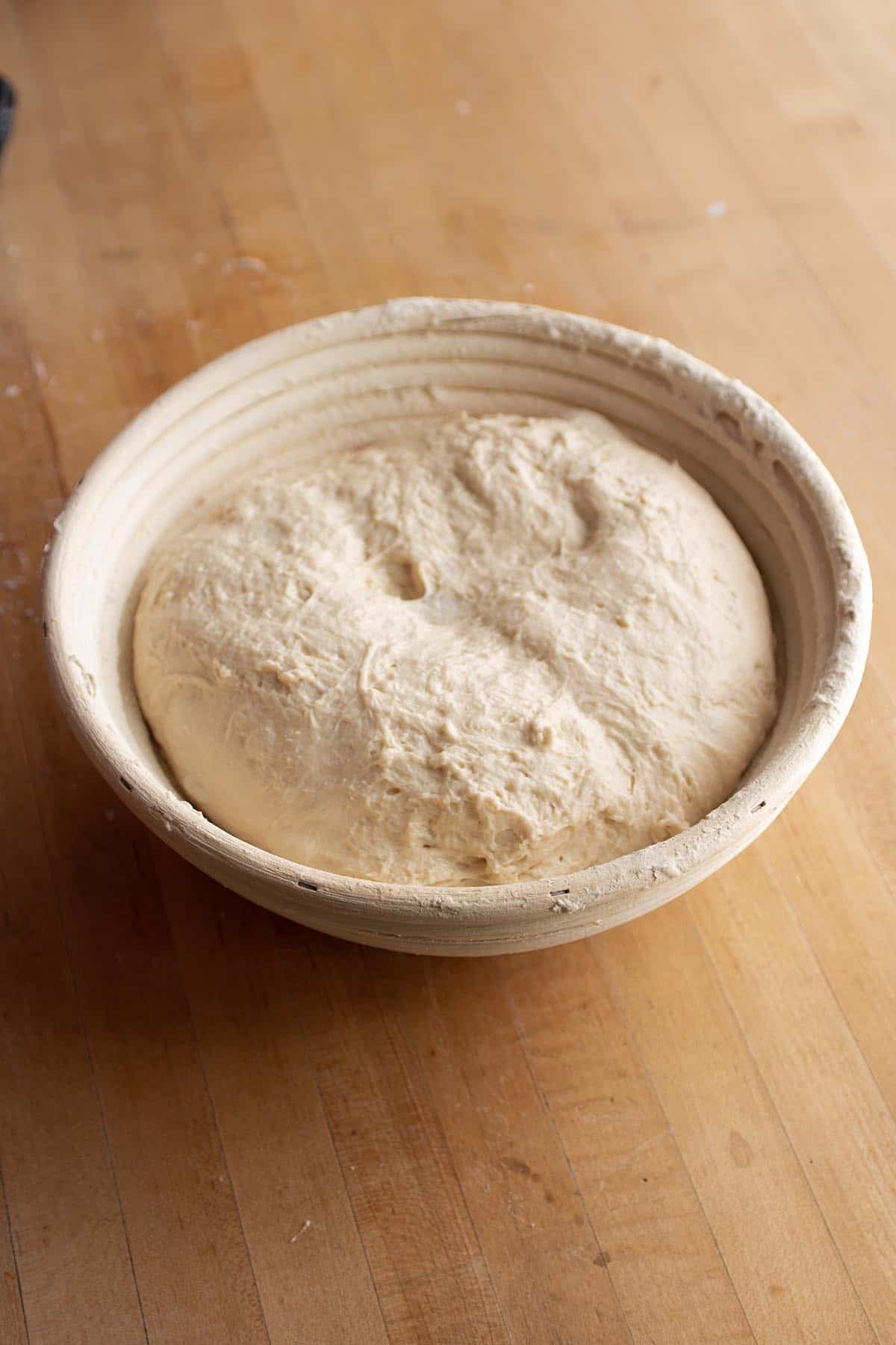 A banneton basket with a loaf of sourdough bread proofing. 