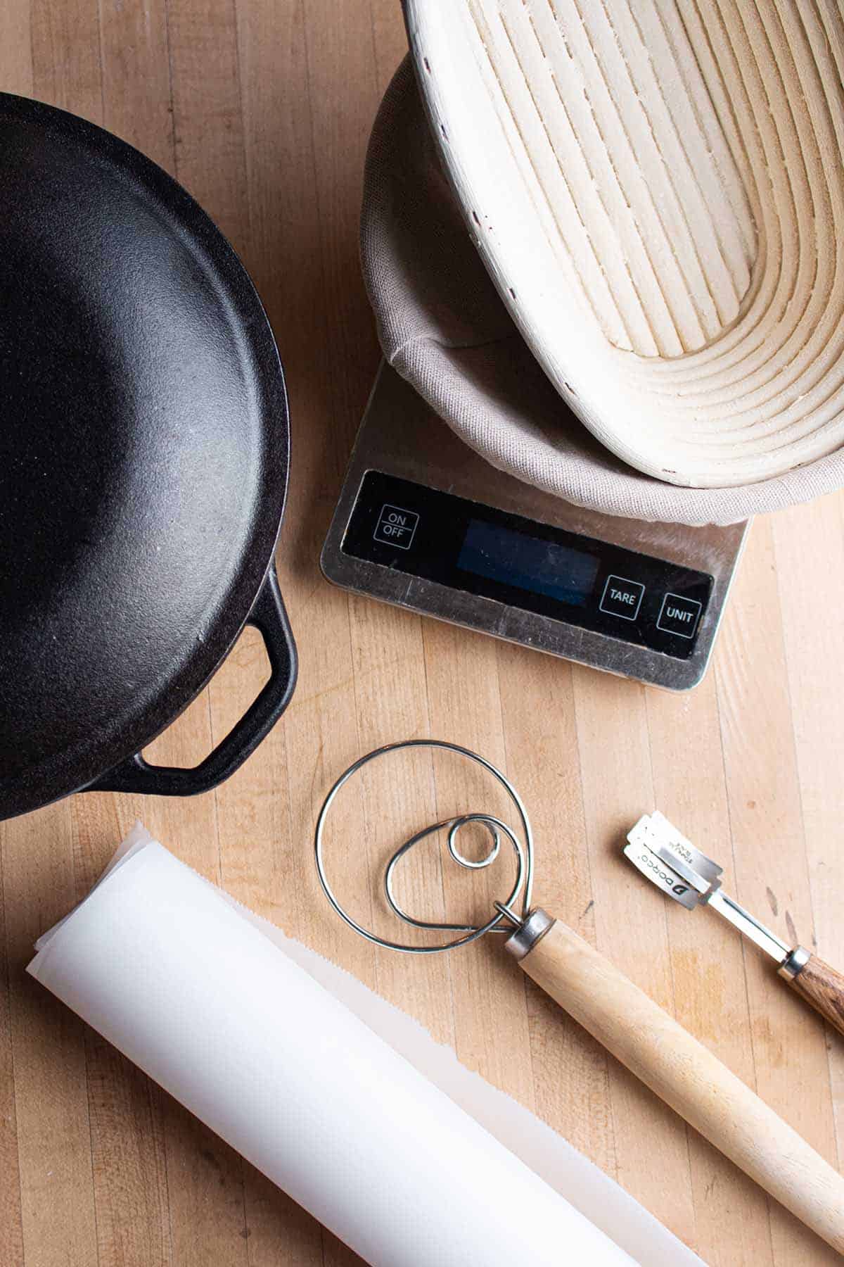 A Dutch Oven, banneton proofing baskets, parchment paper, dough whisk and bread lame.