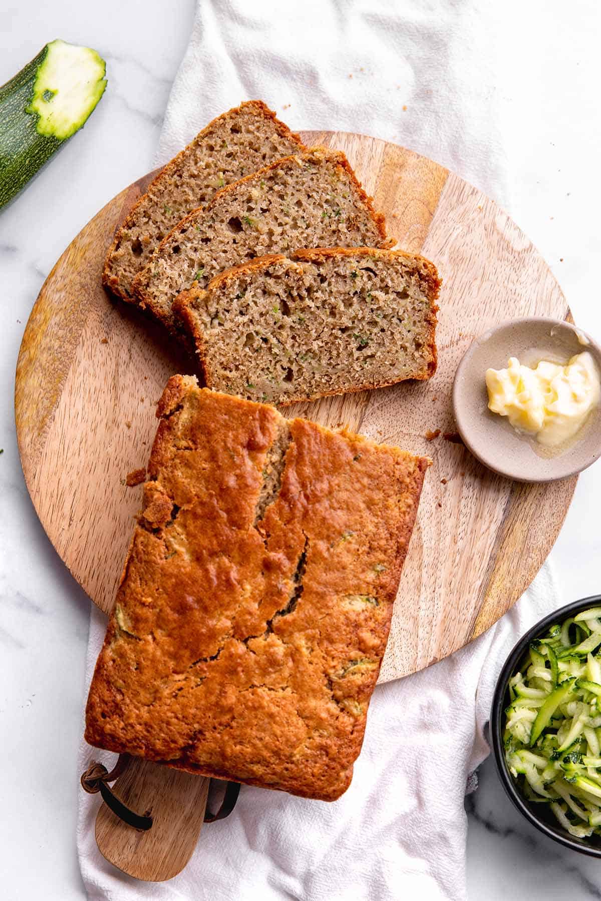A loaf of zucchini bread sitting on a wooden board with shredded zucchini.