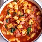 A large white Dutch Oven full of a soup made with tortellini, sausage and spinach.