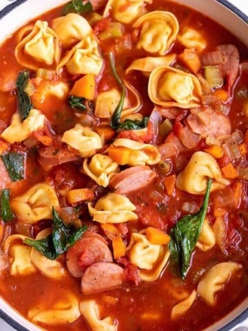A large white Dutch Oven full of a soup made with tortellini, sausage and spinach.