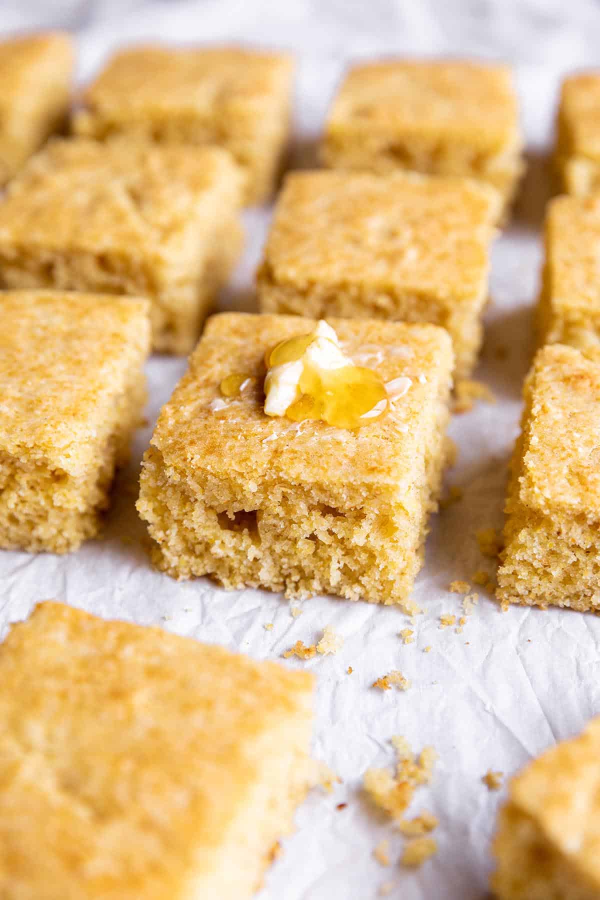 Cornbread cut into squares with some butter and honey.