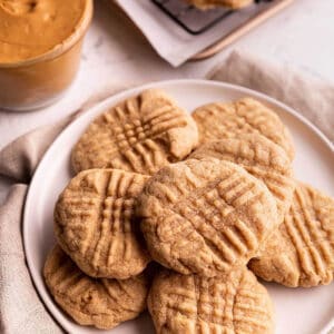 A plate of cookies with a jar of peanut butter in the back.
