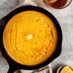 A castiron pan with baked cornbread and butter on top.