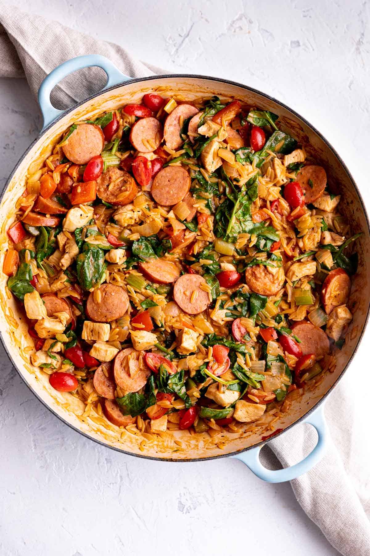 A braiser pan with a mix of chicken, sausage, orzo pasta and spinach. 