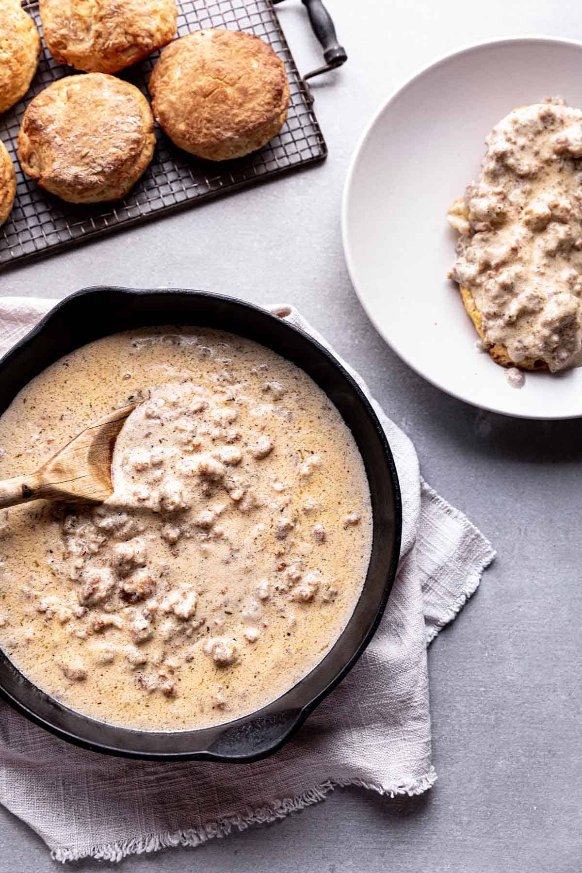 A pan with sausage gravy, a cooling rack with biscuits and a plate of biscuits and gravy.